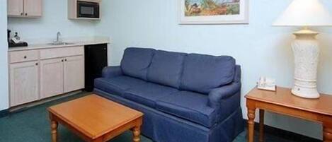 A compact living space with a blue sofa, wooden coffee table, kitchenette with cabinets, and a painting on the wall.