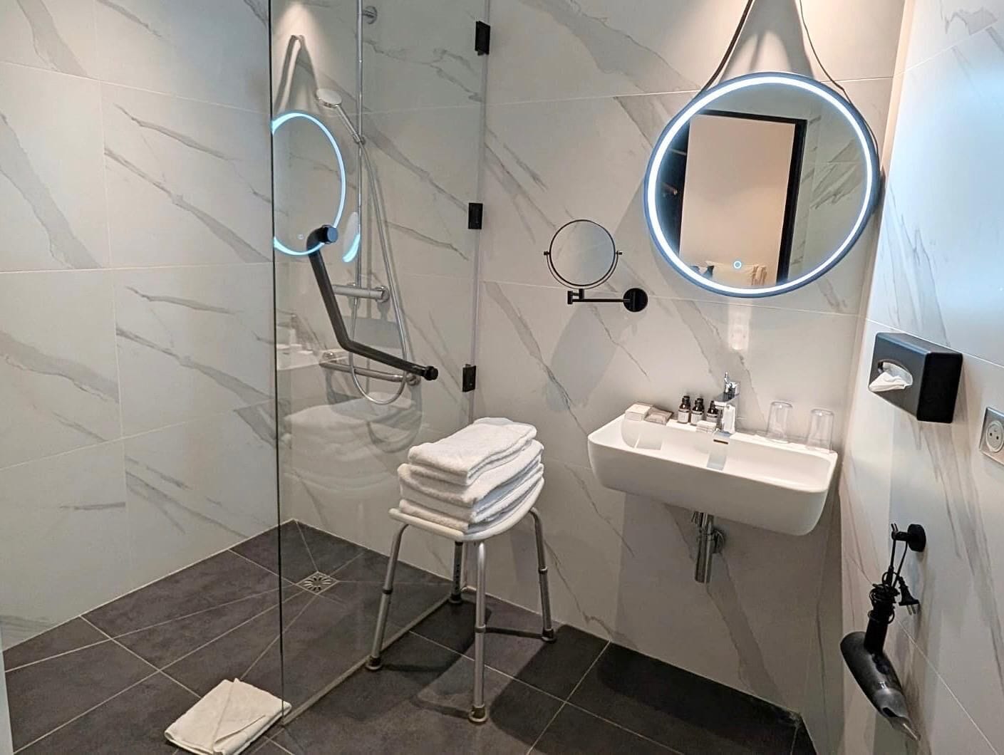 Un baño moderno con cabina de ducha de vidrio, lavamanos con espejo y toallero.