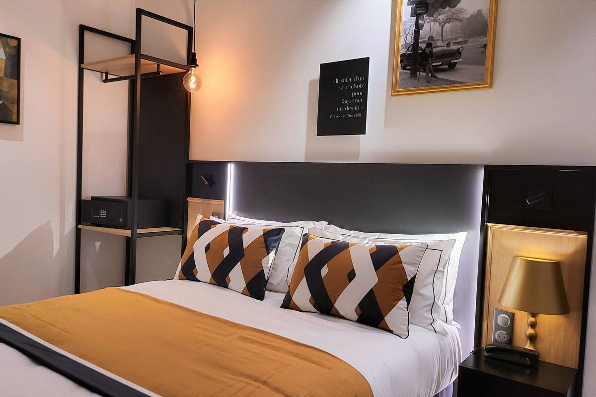 Una habitación de hotel moderna con una cama, una mesita de noche con una lámpara, un estante en la pared y una cita enmarcada.