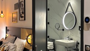 A modern hotel room with a bed, bedside lamps, a large mirror, a sink, and a chair. - Star Champs Elysées (Paris)