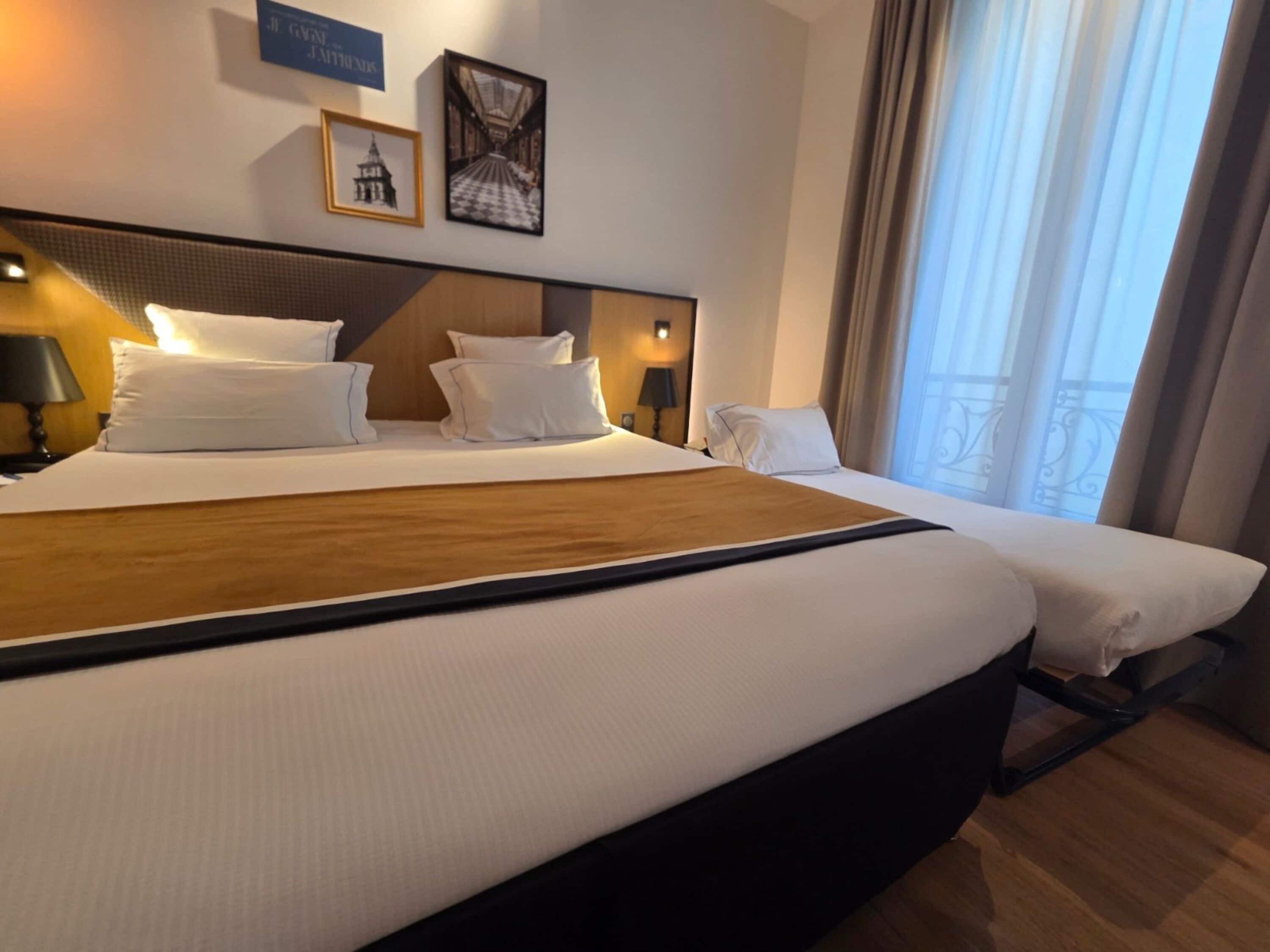 A hotel room with a large bed, two bedside tables, a nightstand, and a window with curtains.