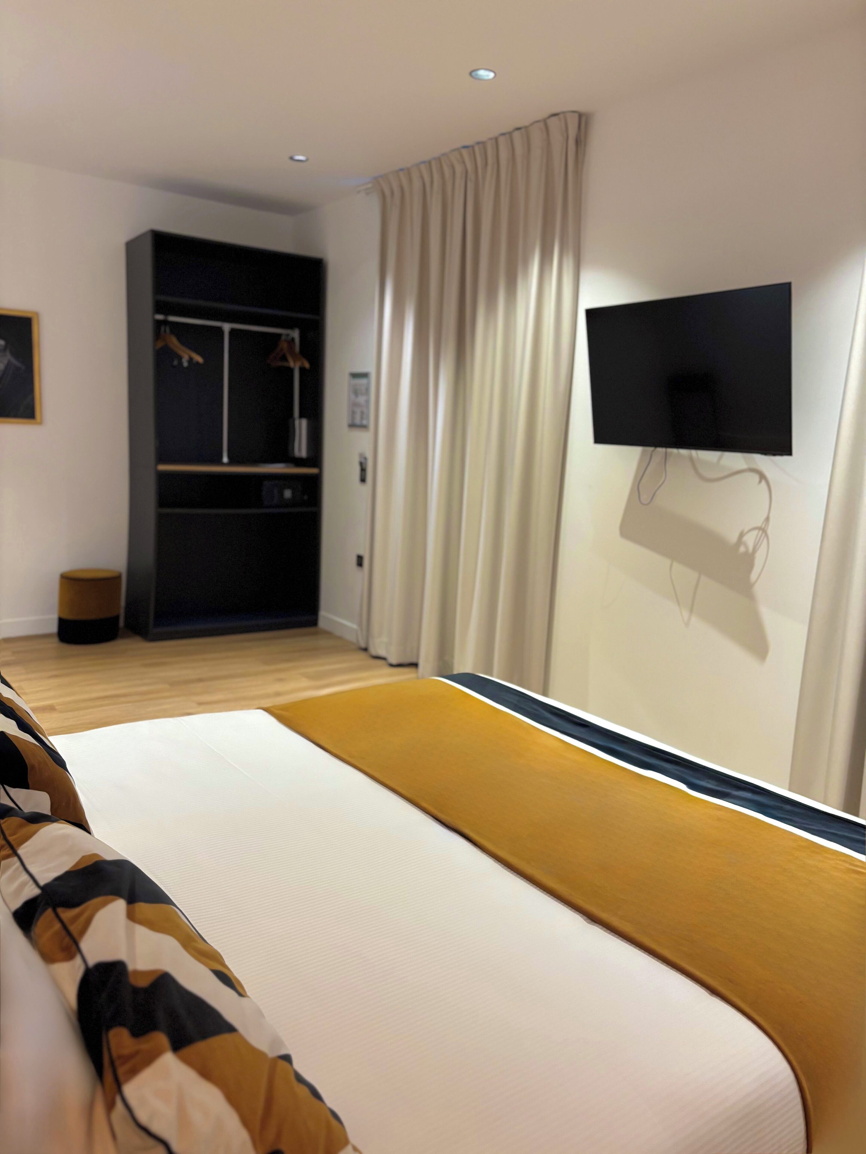 Een moderne hotelkamer met een groot bed, een garderobe, een aan de muur bevestigde televisie en een raam met gordijnen.