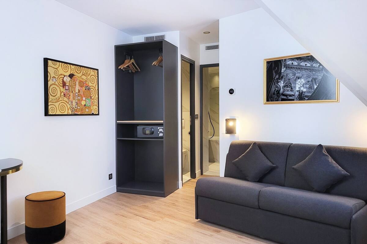 Una sala de estar moderna con un sofá gris, una mesa de centro y un sillón amarillo. Hay un mueble negro con un panel de control y un perchero colgado.