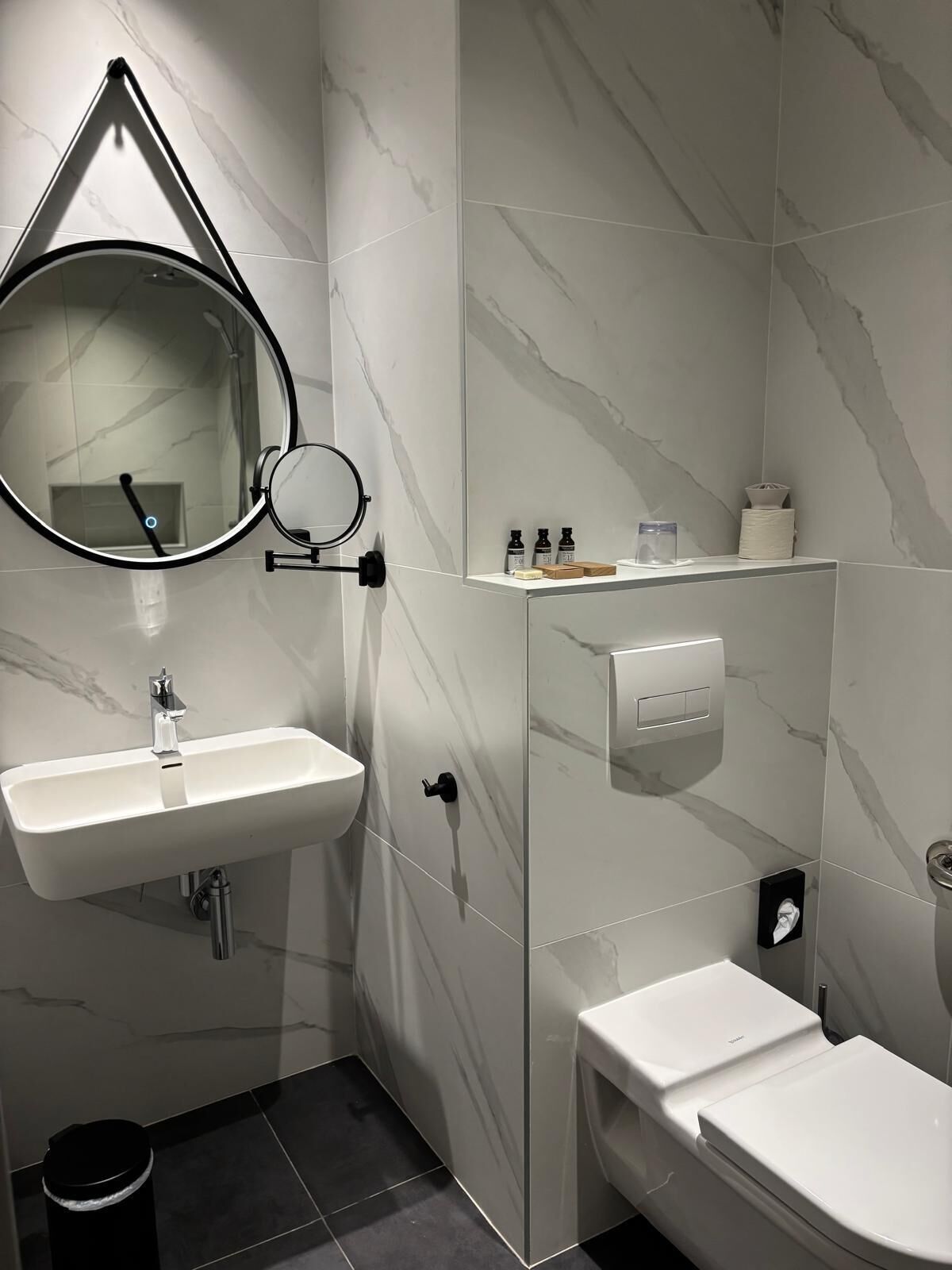 A modern bathroom with a white sink, a mirror, and a toilet.