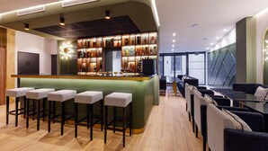 A modern bar area with a green bar counter, multiple stools, and a variety of bottles. - Star Champs Elysées (Paris)
