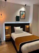 Une chambre d’hôtel moderne avec un grand lit, deux lampes de chevet, un luminaire fixé au mur et un cadre contenant une citation.