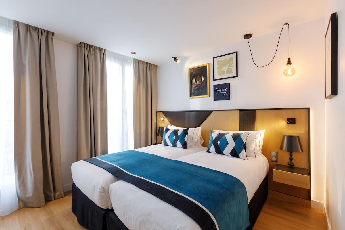 Habitación de hotel con una cama grande, una mesita de noche con lámpara y una lámpara de pared.