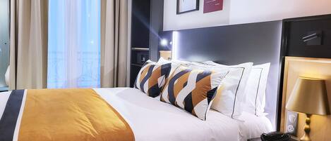 Una habitación de hotel con una cama, almohadas, una mesita de noche con lámpara y una pared con cuadros enmarcados.