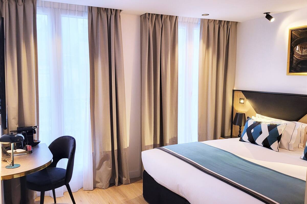Una habitación de hotel con cama, escritorio y silla, y cortinas.