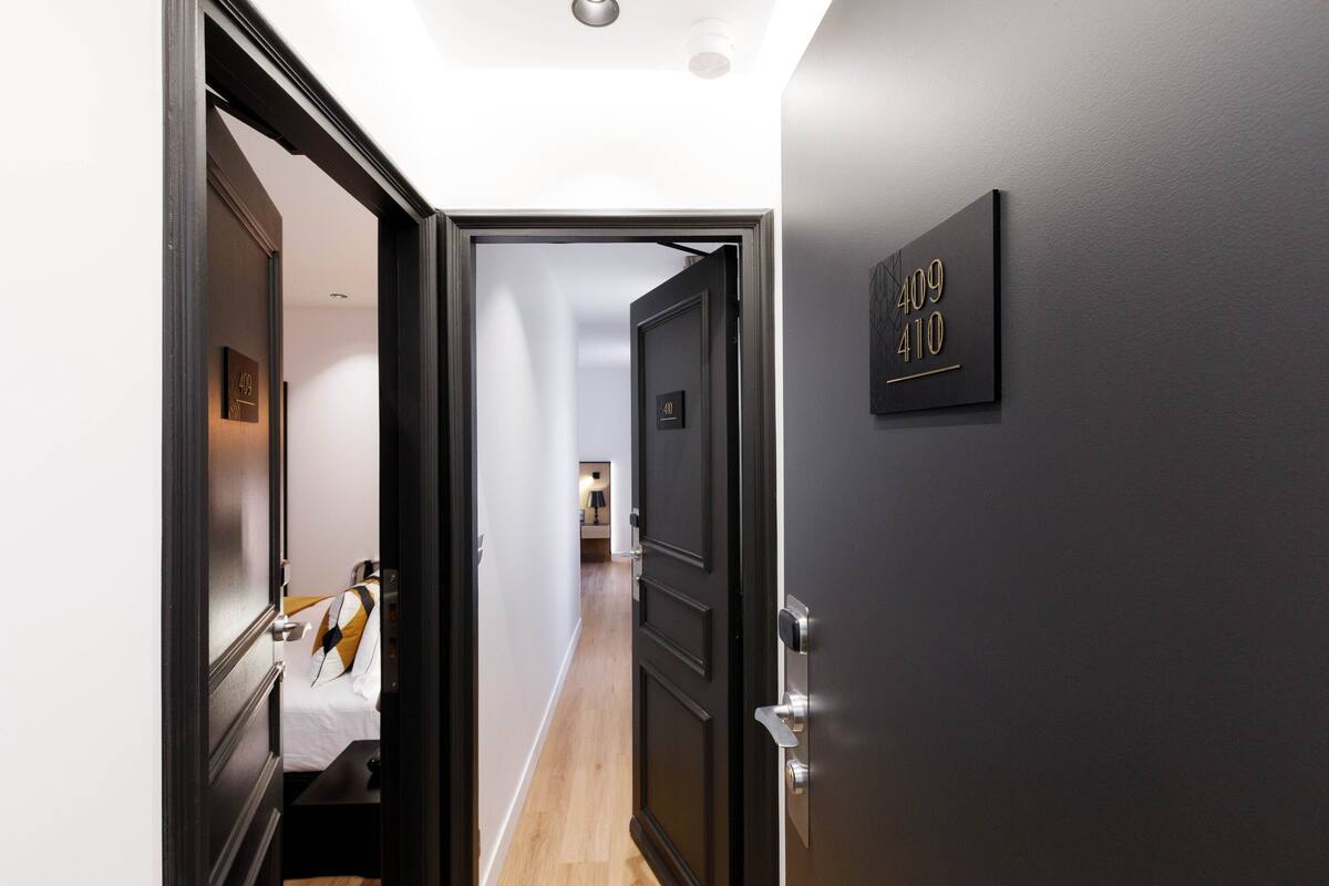 Un pasillo con una puerta que da a un dormitorio. El pasillo tiene un interruptor de luz y una placa de número en la pared que indica los números de habitación.