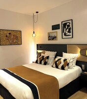 A modern hotel room with a large bed, a headboard, a bedside table with a lamp, and artwork on the walls.