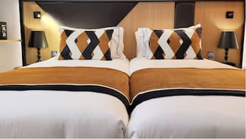 Een hotelkamer met een groot bed, twee kussens met een diamantmotief en twee nachtlampjes.