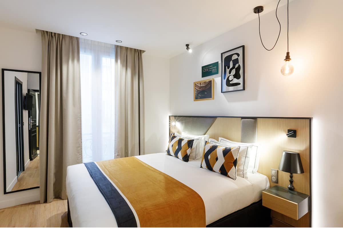 Una habitación de hotel moderna con una cama grande, una mesita de noche con lámpara y un espejo.