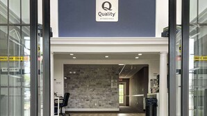 L’entrée d’un hôtel, avec une enseigne « Quality by Choice Hotels », un comptoir d’accueil, un mur en pierre et un paillasson noir à l’entrée.