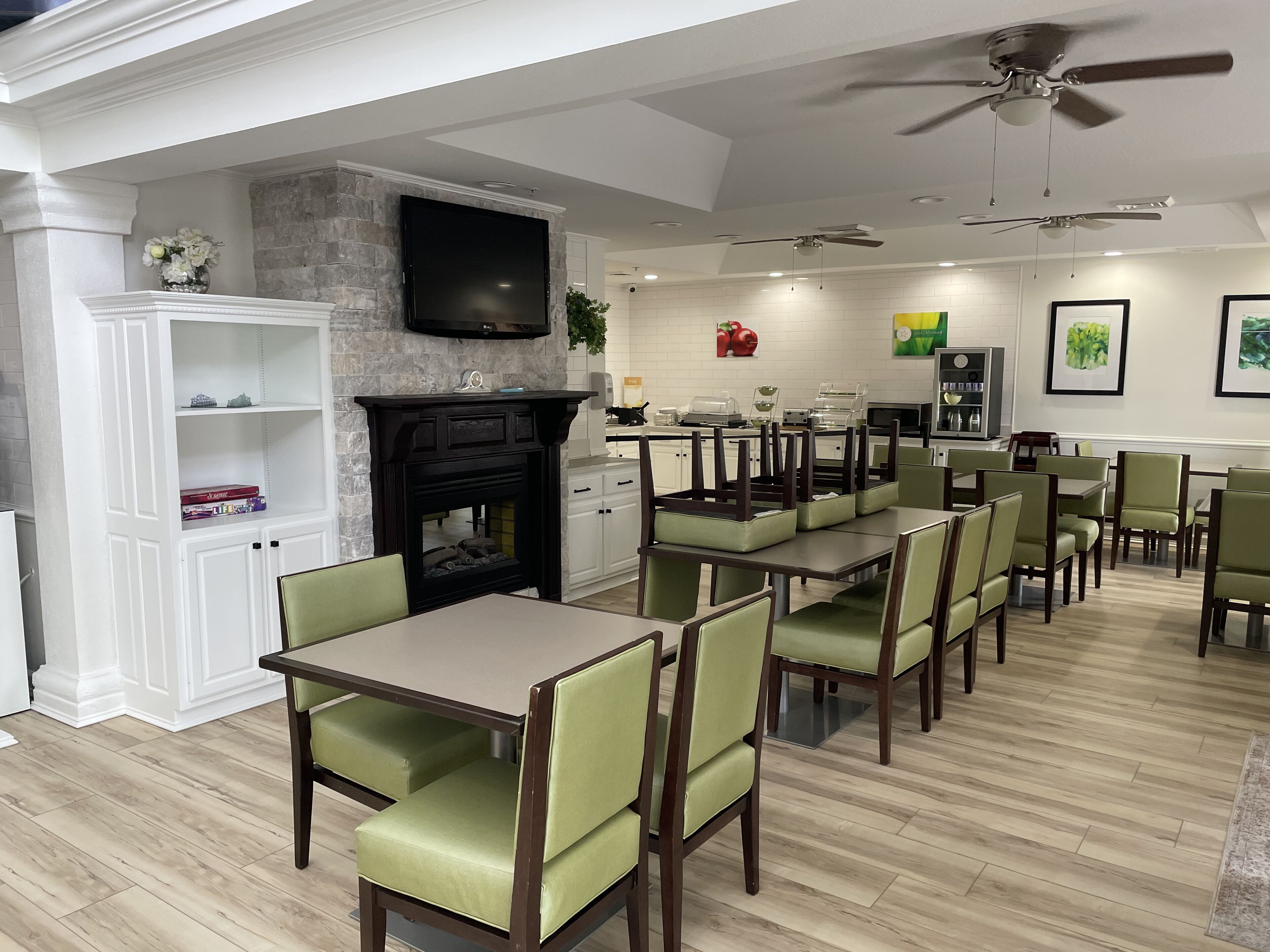 A dining area with tables and chairs, a fireplace, a television, and ceiling fans.