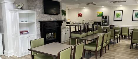 A dining area with tables and chairs, a fireplace, a television, and ceiling fans.