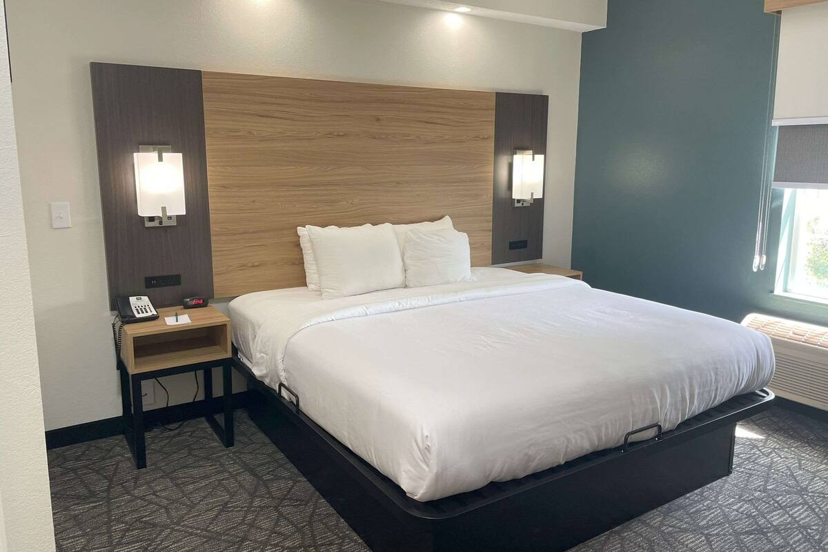 Una habitación de hotel con una cama grande, mesitas de noche, un teléfono y un reloj.