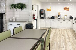 A modern kitchen with white cabinets, a coffee station, and a dining area with a table and chairs.