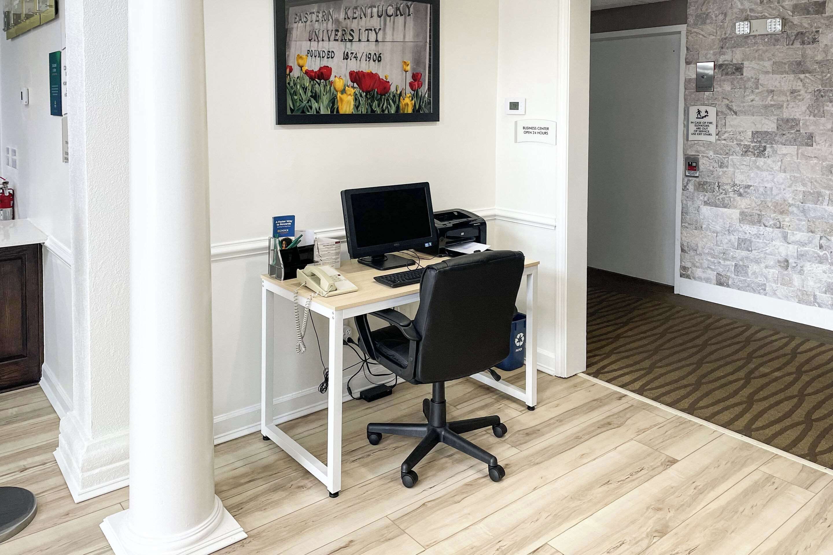 A modern office space with a desk, computer, and office chair. There is a framed picture on the wall and a door to the right.