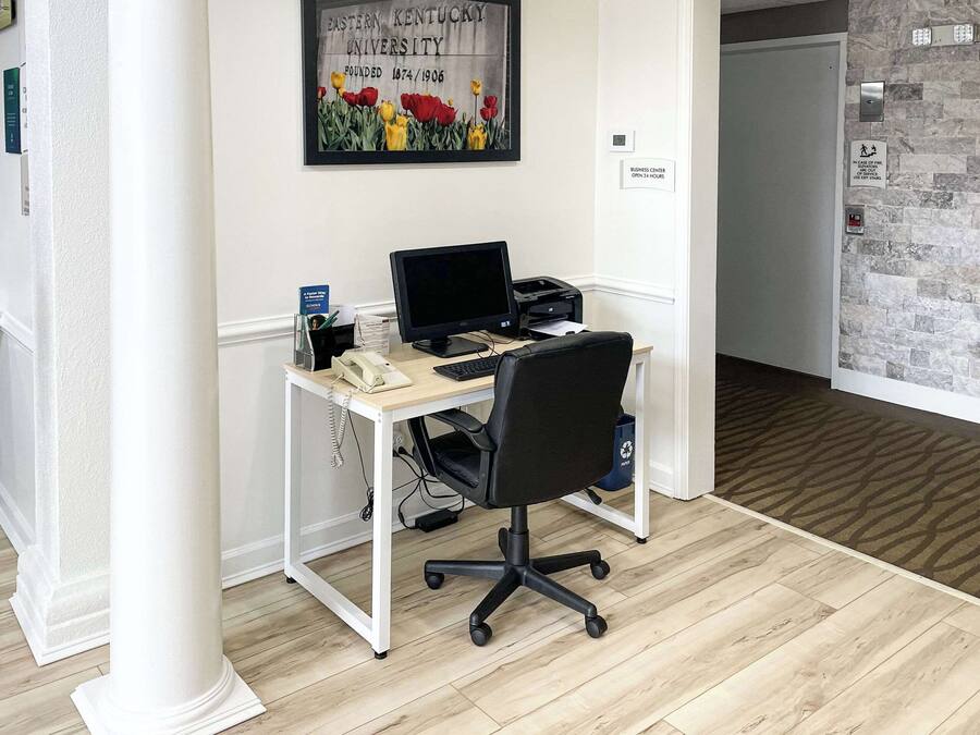 A modern office space with a desk, computer, and office chair. There is a framed picture on the wall and a door to the right.