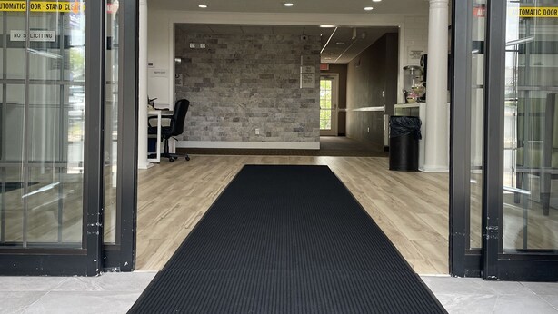 L’entrée d’un hôtel, avec une enseigne indiquant « Qualité garantie par Choice Hotels », un comptoir d’accueil, un mur en pierre et un tapis noir menant à l’intérieur.