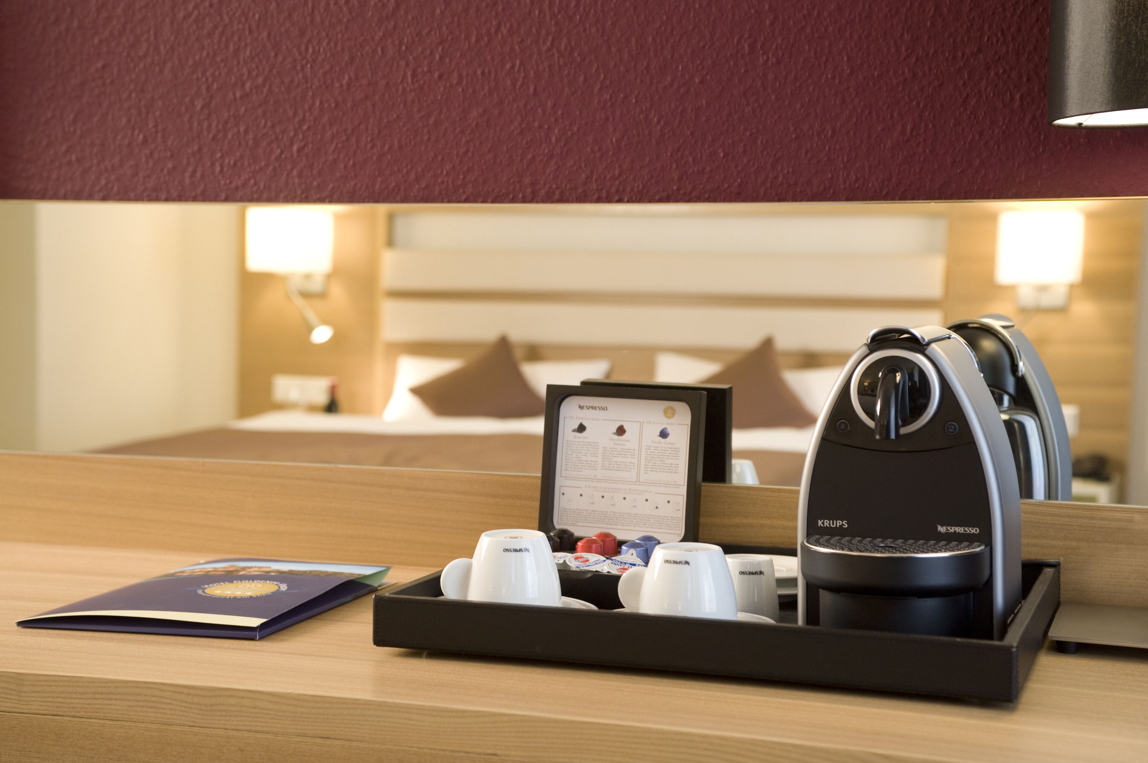 A hotel room with a wooden desk, a Krups espresso machine, a menu, and a tray with cups and a small box.