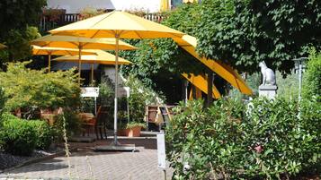Un espace extérieur aménagé avec des parasols jaunes, une statue et des plantes en pot.
