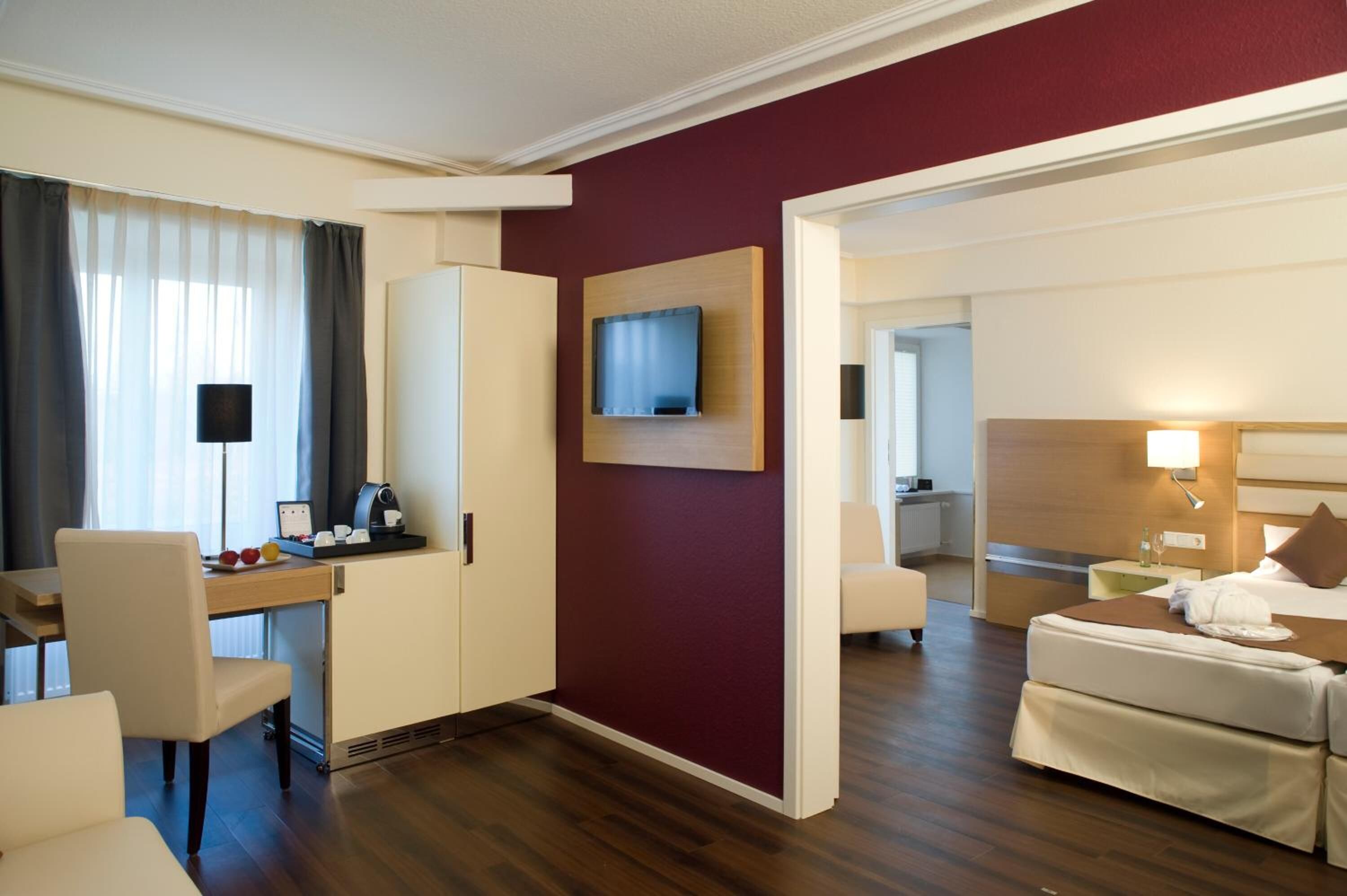 Een hotelkamer met een bureau, stoel, bed en een aan de muur bevestigde televisie.