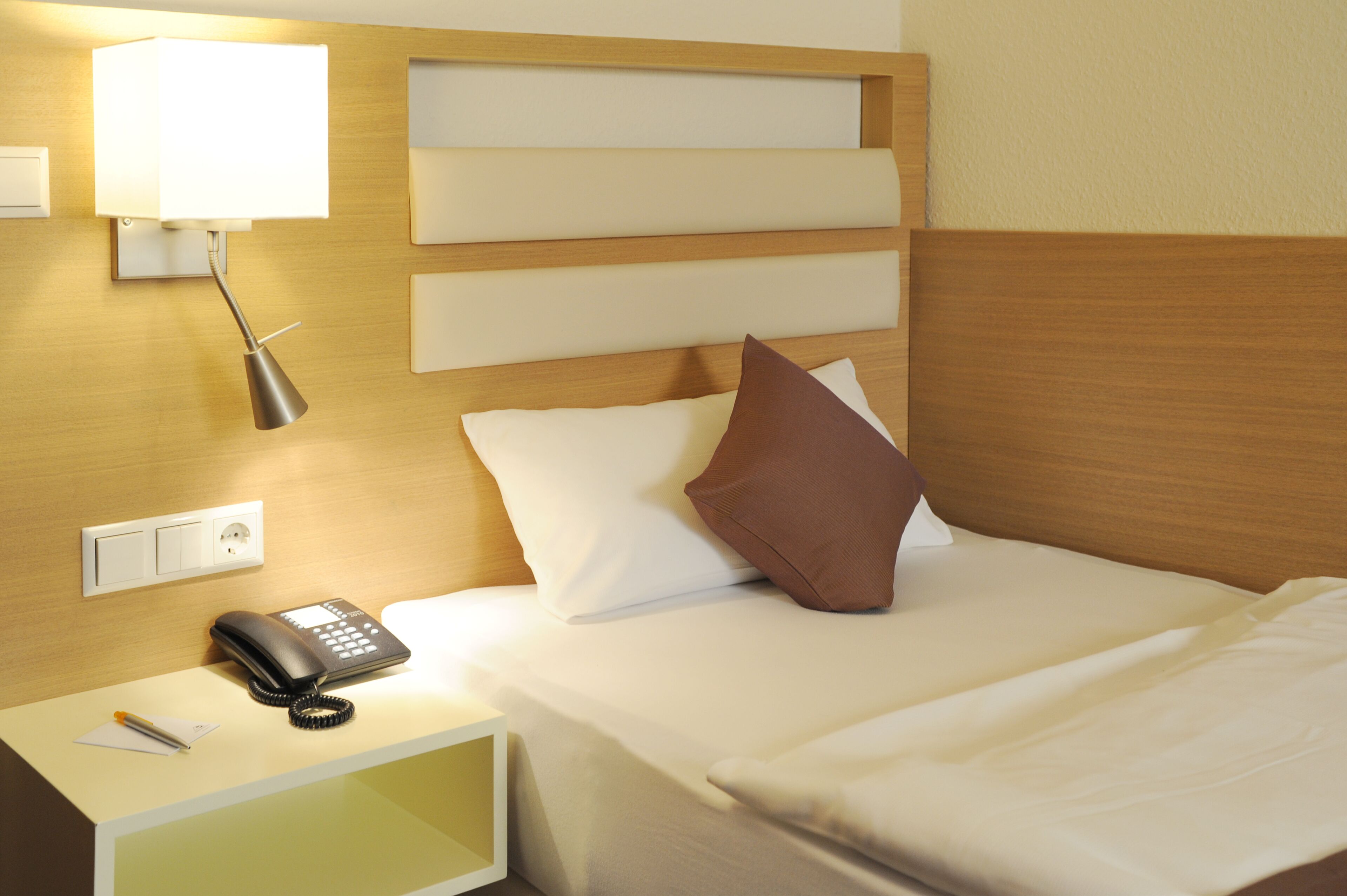 A hotel room with a bed, a bedside lamp, a phone, and a nightstand.