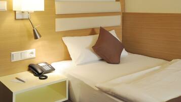 A hotel room with a bed, a bedside lamp, a phone, and a nightstand.