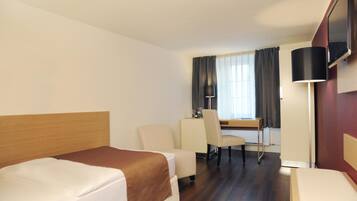 A hotel room with two beds, a desk, a chair, a lamp, and a TV.