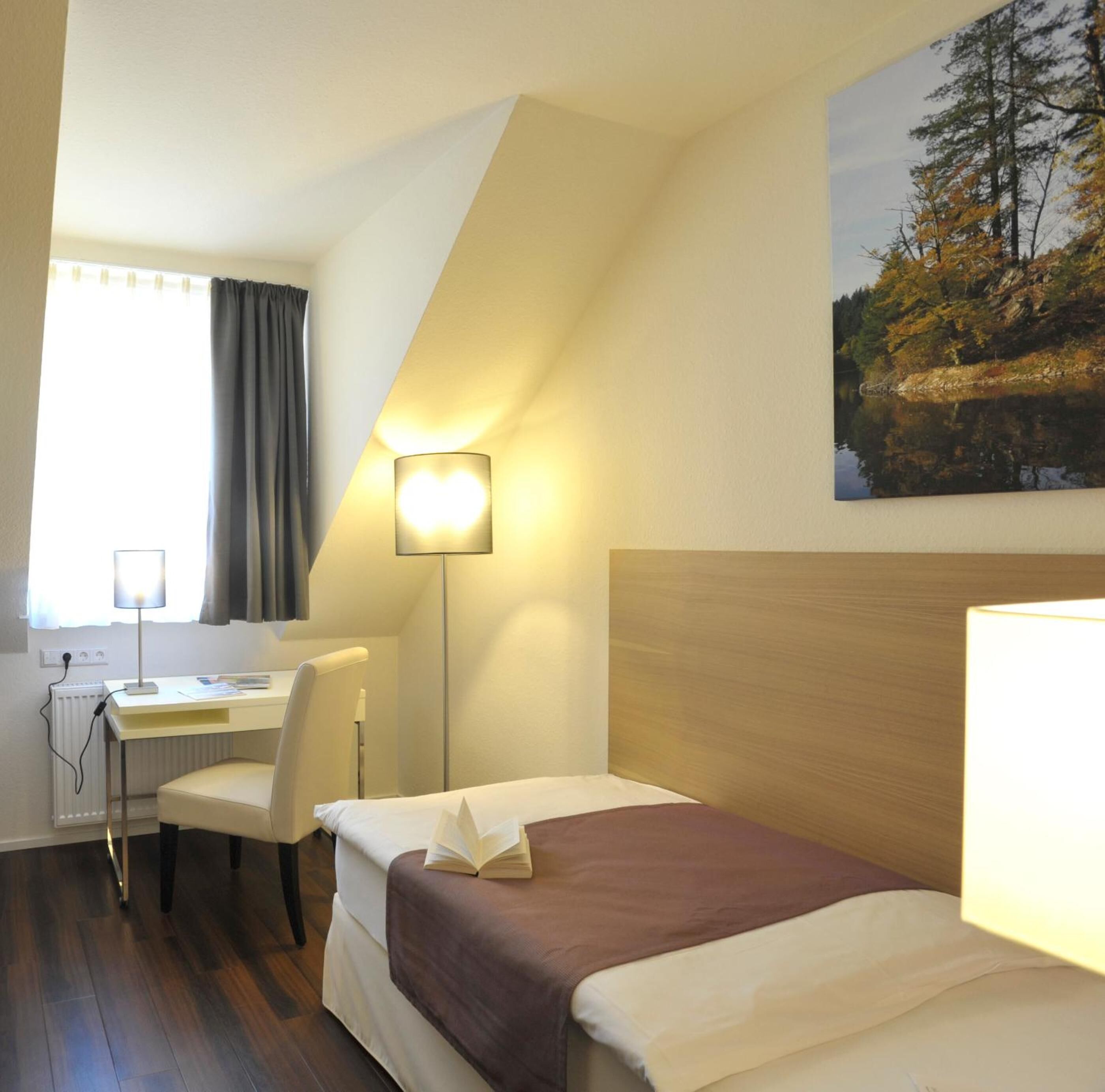 Ein Hotelzimmer mit einem Bett, einem Schreibtisch, einem Sessel und einem Bild von einem Wald.