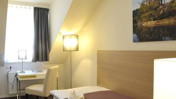 Ein Hotelzimmer mit einem Bett, einem Schreibtisch, einem Sessel und einem Bild von einem Wald.