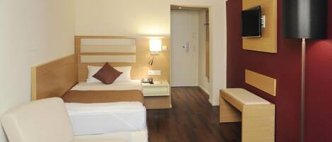 A hotel room with a bed, bedside table, lamp, TV, and a bench.