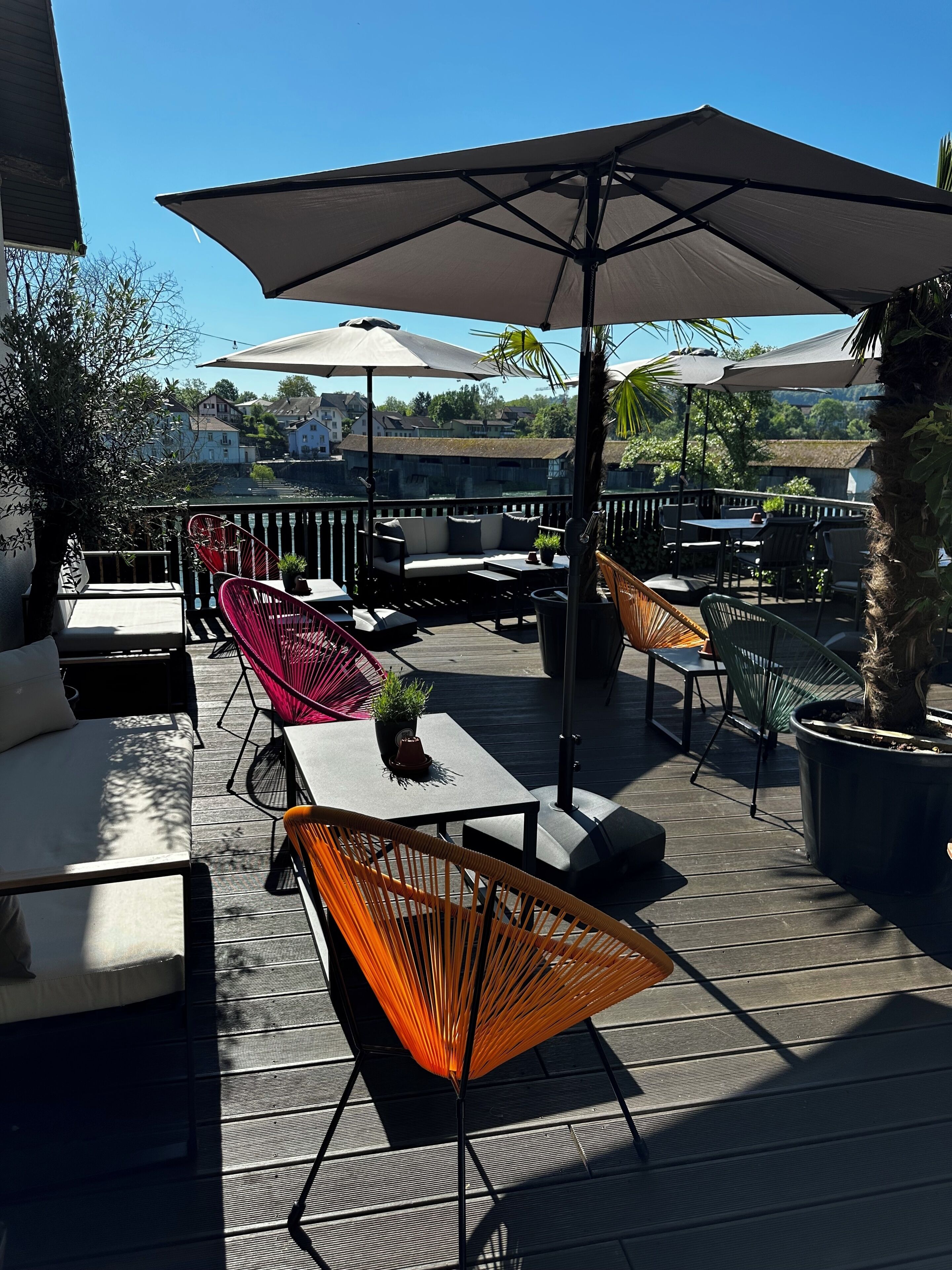A deck with outdoor furniture, including a sofa, chairs, and tables, under large umbrellas.