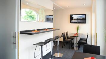 Une chambre d’hôtel moderne dotée d’un coin repas, d’un téléviseur fixé au mur et d’une fenêtre donnant sur un paysage verdoyant.