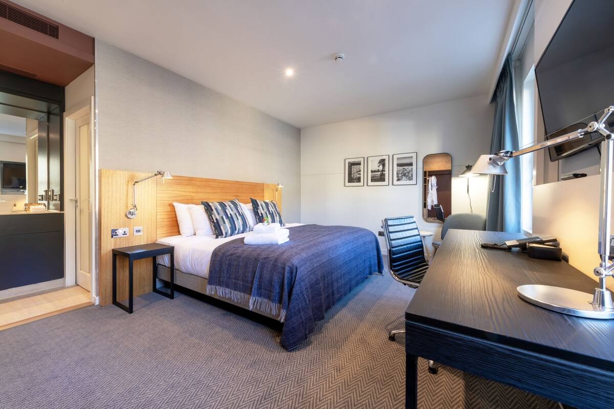 A modern hotel room with a large bed, a desk, and a television.