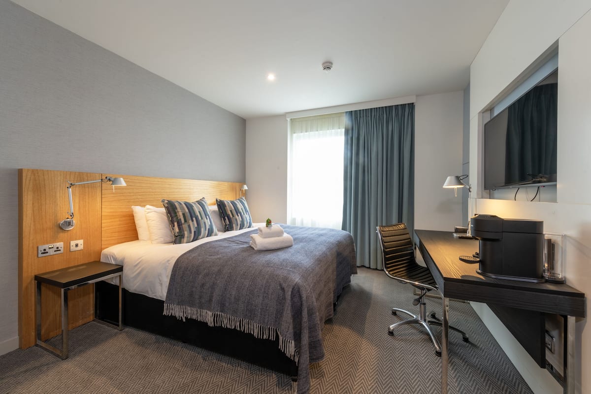 A hotel room with a bed, desk, and television.