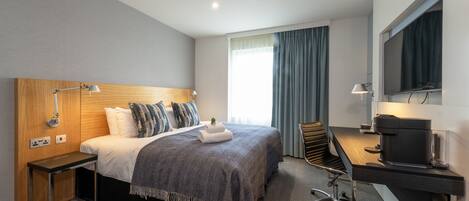 A hotel room with a bed, desk, and television.