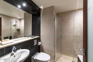 Une salle de bain moderne dotée d’un grand miroir, de deux lavabos, de toilettes et d’une douche à parois de verre.