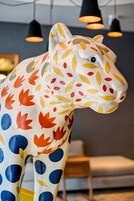 A colorful animal sculpture with a leaf pattern, positioned in a room with modern lighting fixtures and a minimalist design.
