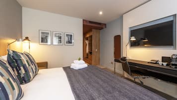 A modern hotel room with a large bed, a desk with a computer, a chair, and a wardrobe.