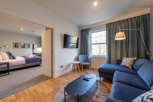 A modern hotel room with a bed, a sofa, a small table, and a TV.