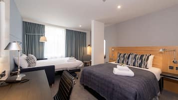 Ein Hotelzimmer mit zwei Betten, einem Schreibtisch, einem Stuhl, einer Lampe und einem Nachttisch.