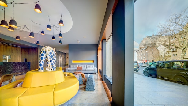 En modern entréhall med en gul sittgrupp, en soffa och en skulptur med ett intressant mönster.
