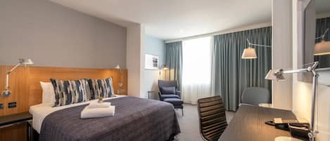 A hotel room with a large bed, a desk, a chair, a lamp, and a window with curtains.