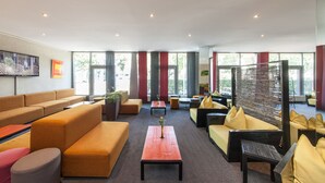 Un vestíbulo amplio con varias zonas de estar, incluyendo sofás y sillones, una mesa de centro y grandes ventanales que aportan luz natural.