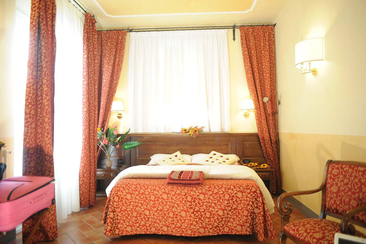 A hotel room with a bed, a chair, a nightstand, and a window with curtains.