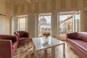 A spacious living room with a glass coffee table, two leather sofas, and a view of a dome and buildings through large windows.