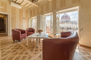 A spacious room with a large window offering a view of a dome and a terrace. There is a white table and two red chairs.